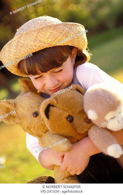 park-scene, portrait, half-figure, 8-year-old girl wearing white blouse and strawhat hugging her 3 softtoys on a green-yellow meadow  - GERMANY, 01/04/2004