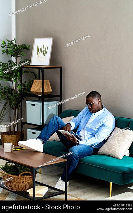 Male professional using digital tablet while sitting on sofa at home