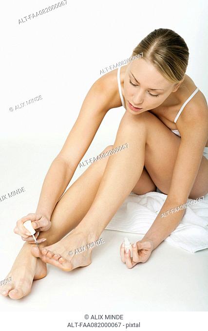 Young woman sitting on floor in her underwear, painting her toenails