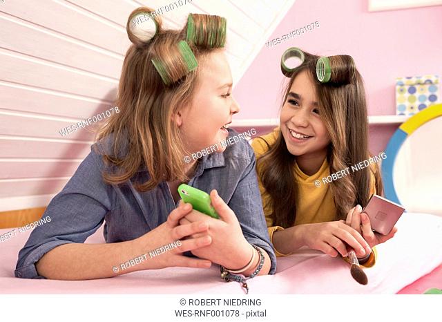 Girls with hair rollers lying and watching smartphone, smiling