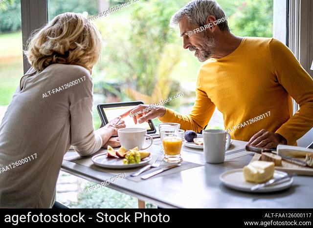 Mature couple using digital tablet while having breakfast at home
