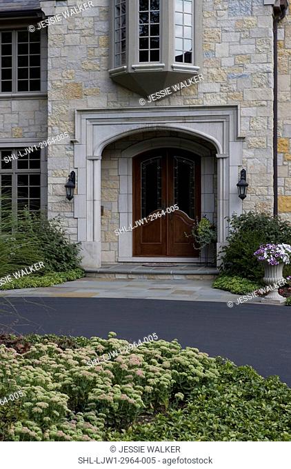 EXTERIORS: Blacktop driveway to French Normandy stone home, close up of double door entry limestone arch outdoor lighting
