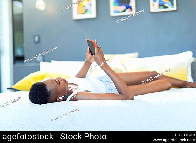 Young woman relaxing on bed, listening to music with mp3 player and headphones