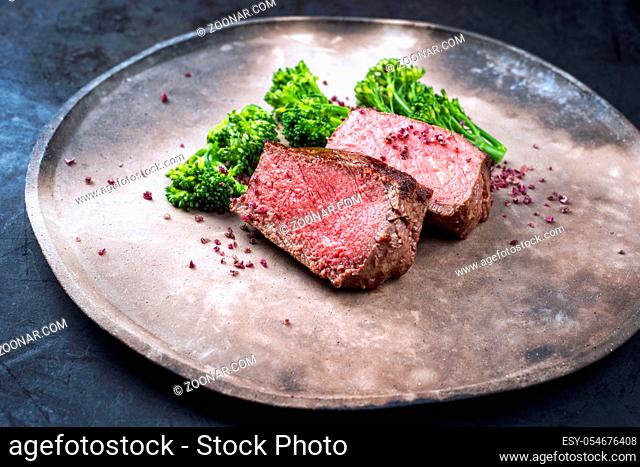 Barbecue dry aged wagyu roast beef natural sliced offered with rapini and salt as closeup on a modern design plate