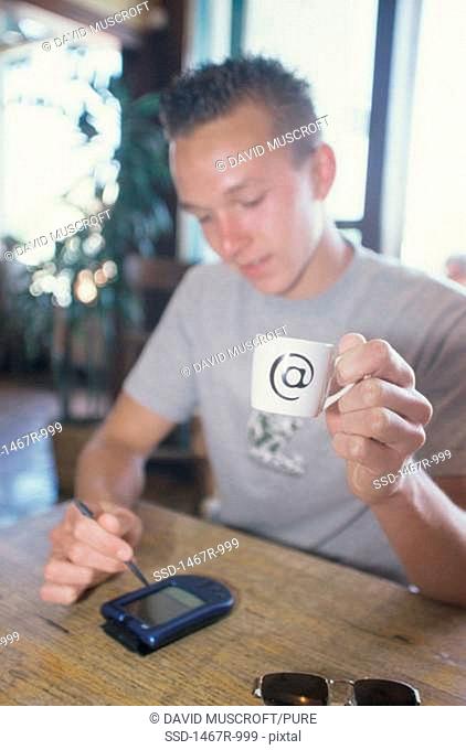 Young man holding a cup and writing on a hand held device