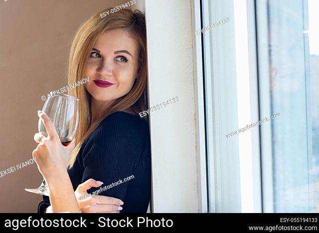 portrait of a girl with a smile looking out the window with a glass of wine