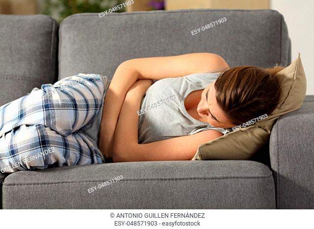 Teen suffering belly pms symptoms lying on a sofa in the living room at home