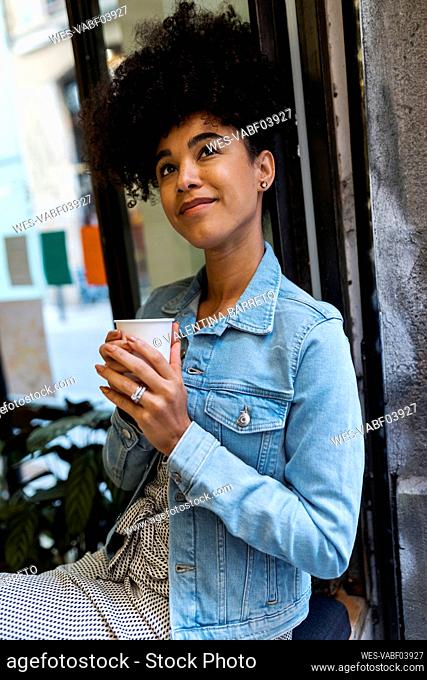 Mid adult woman with coffee cup looking up while sitting by window at cafe