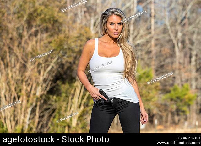 A beautiful blonde model holds a pistol for protection on a sunny day