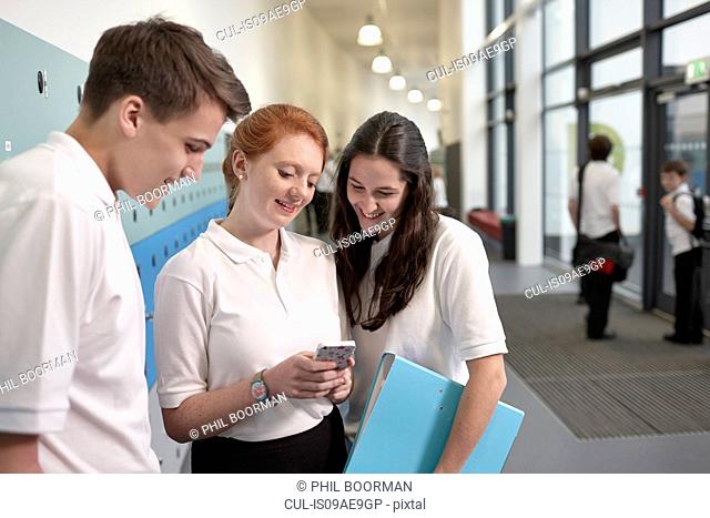 Teenagers looking at mobile phone in school corridor