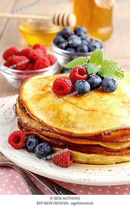 Stack of pancakes with syrup, raspberries and blueberries decorated with mint leaf. Party dessert