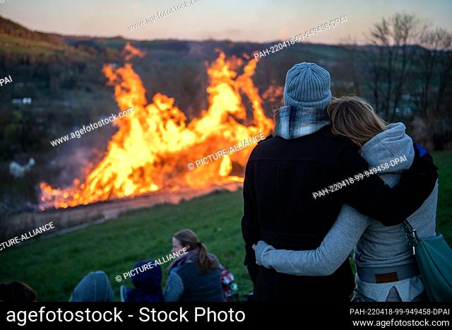 17 April 2022, North Rhine-Westphalia, Lügde: A couple stands by an Easter fire. When it is dark the straw in the wheels is lit and the wheels are pushed down...
