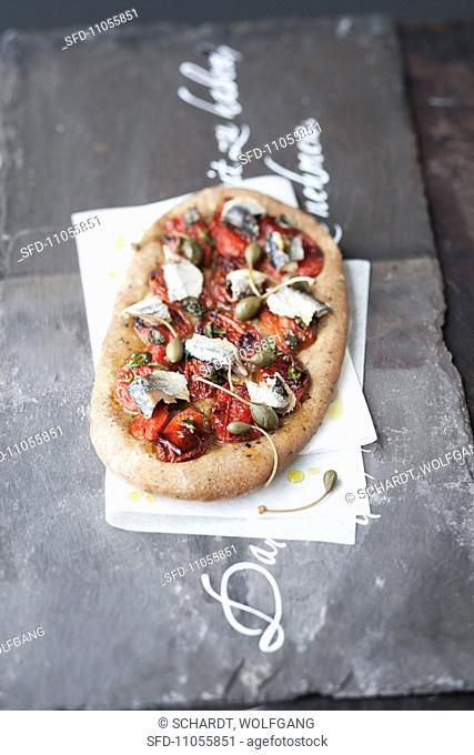 A pizza topped with oven-baked tomatoes and sardines