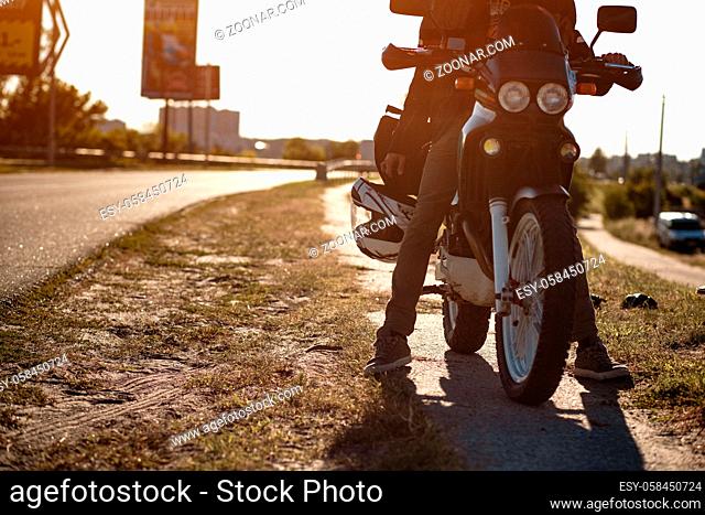 Close view on the legs of a motorcyclist on the motorcycle on an empty road at sunny day