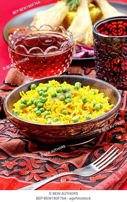 Indian cuisine, bowl of yellow rice with green peas on red background