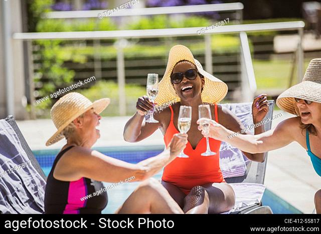 Happy senior women friends drinking champagne at sunny summer poolside