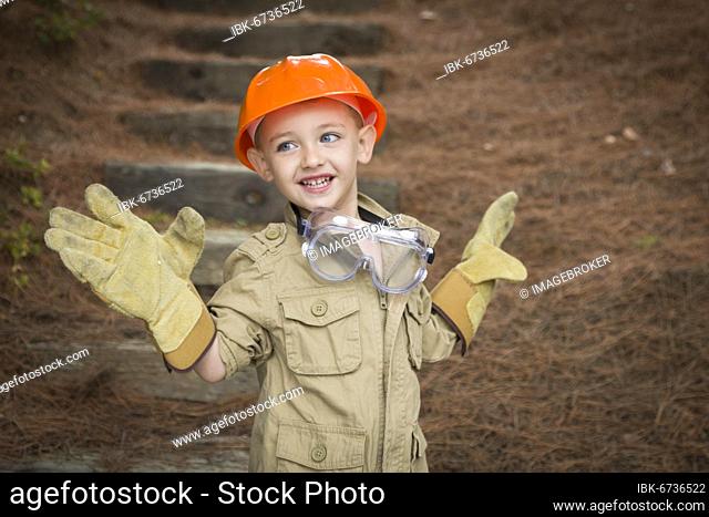 Happy adorable child boy with big gloves, hard hat and goggles playing handyman outside