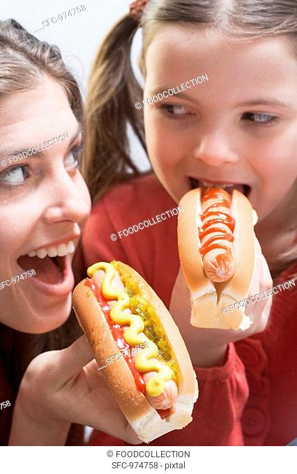Woman and girl eating hot dogs together
