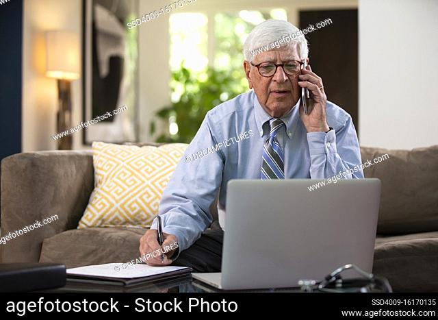 Mature Caucasian Male doctor practicing tele-medicine from his home using laptop computer, Talking to patient and taking notes