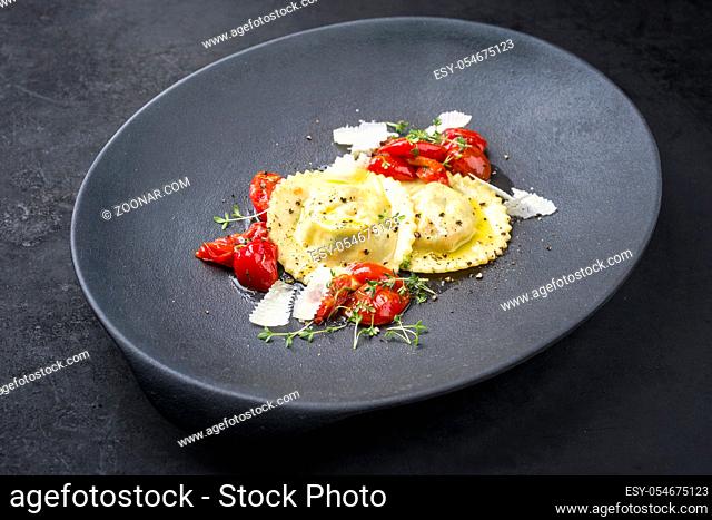 Traditional Italian ravioli pasta offered with parmesan cheese and fried tomatoes as closeup on a modern design plate