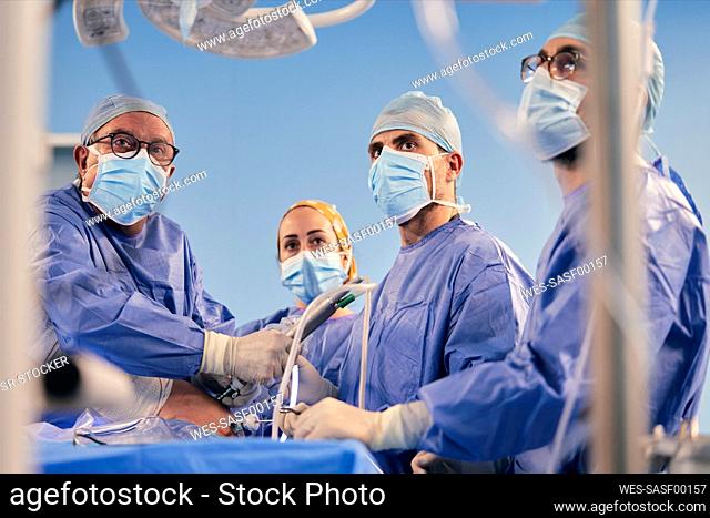 Professionals with endoscope surgical equipment operating surgery while standing in operating room during COVID-19