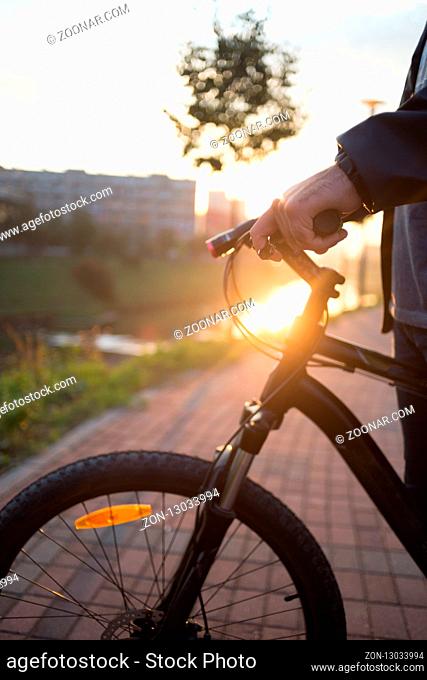 people, travel, tourism, leisure and lifestyle - close up of young hipster man hands holding fixed gear bike wheel on city street - sunset