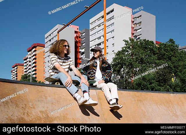 Smiling young man talking with girlfriend sitting on sports ramp
