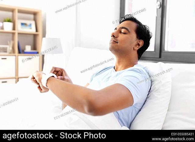 happy indian man with smart watch in bed at home