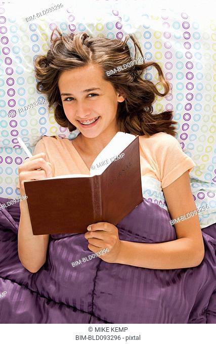 Caucasian teenager laying in bed writing in journal