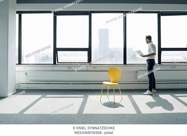 Mature businessman using laptop at the window in empty office