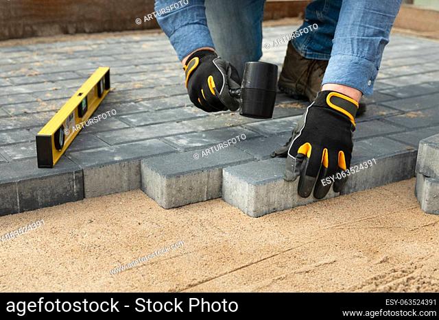 Construction worker laying cement pavement on a walkway with gloves and rubber hammer. House improvement