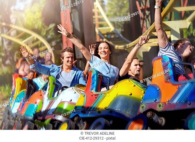 Enthusiastic friends cheering on roller coaster at amusement park