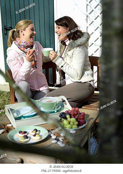 Two women having breakfast on bench and smiling
