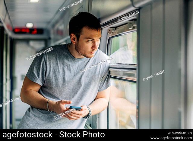 Man holding smart phone leaning on window of railroad car
