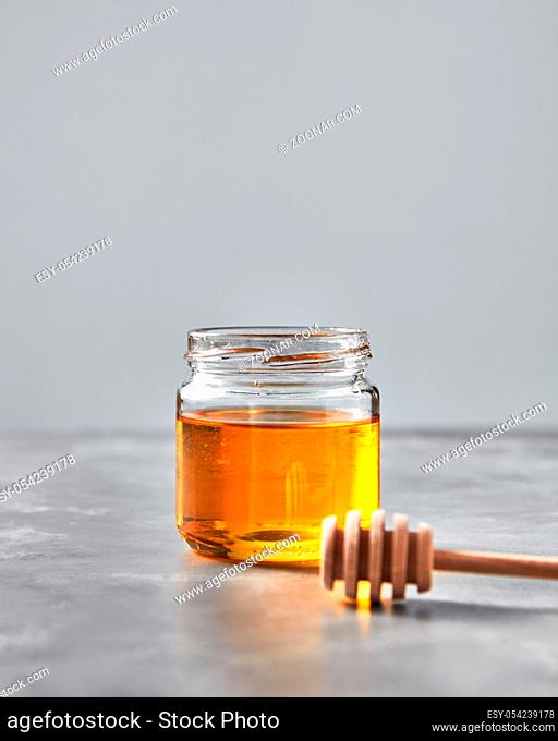 Natural sweet dessert - organic honey in a glass pot with dipper on a gray stone table, copy space. Rosh hashanah jewish concept