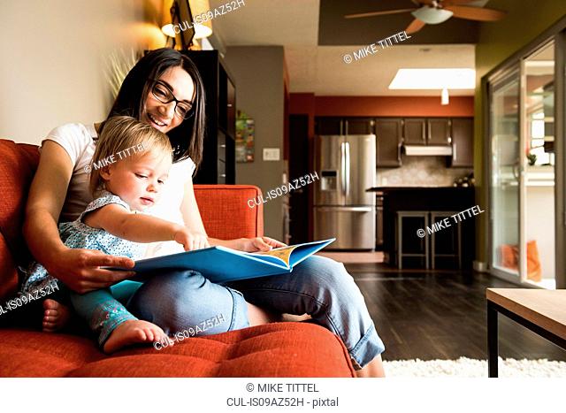 Mother teaching daughter to read book on sofa