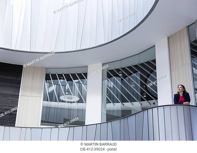 Pensive businesswoman standing on architectural, modern office balcony