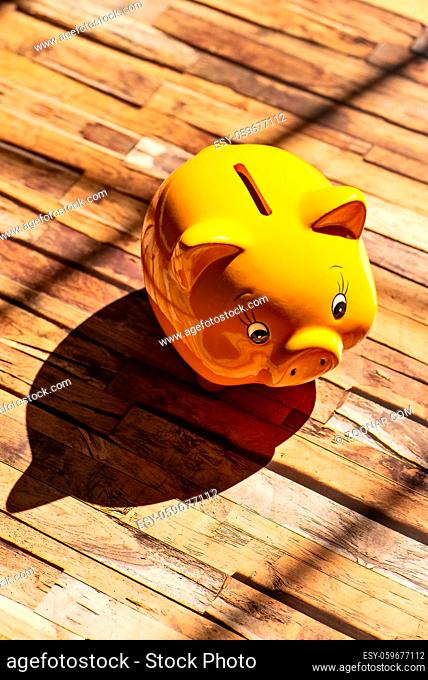 Ein gelbes Sparschwein steht auf einem Holzboden und wirft einen starken Schatten A yellow piggy bank stands on a wooden floor and casts a strong shadow