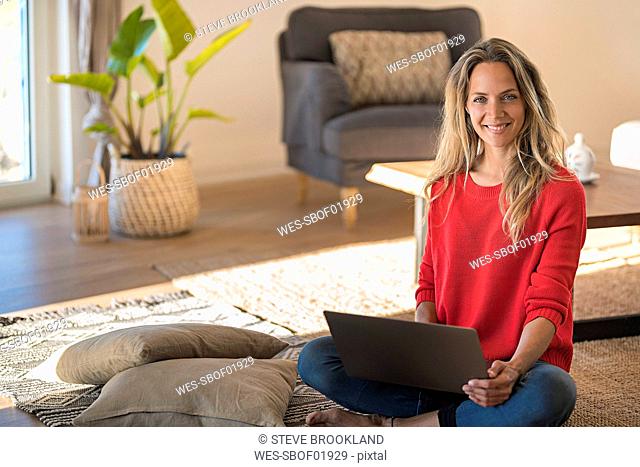 Portrait of smiling woman sitting on the floor at home using laptop