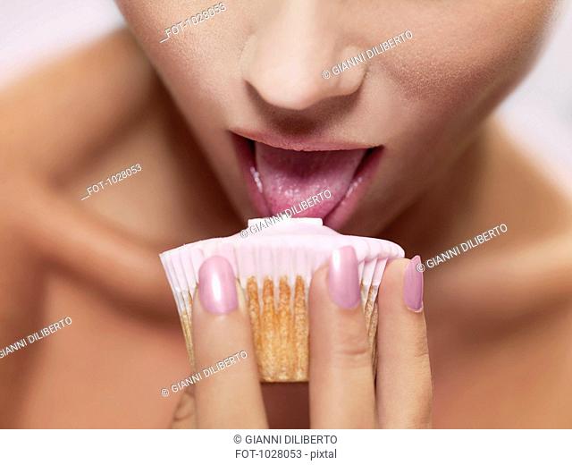 A woman licking frosting on a cupcake, focus on mouth