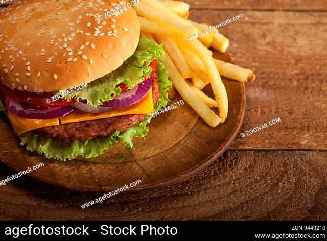 Fresh delicious double burger with cheese, tomato, onion, french fries and lettuce on wooden table with copy space