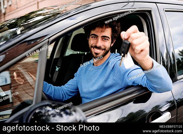 Smiling man holding key sitting in car