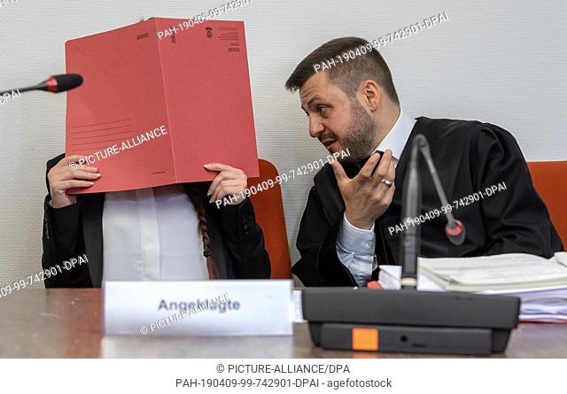 09 April 2019, Bavaria, München: The defendant holds a red file cover in front of her face on her seat in the courtroom. On the right