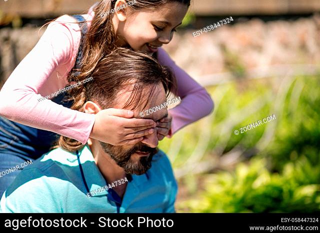 The Girl Is Closeing Her Dad's Eyes With Her Hands And Smiling Outdoors