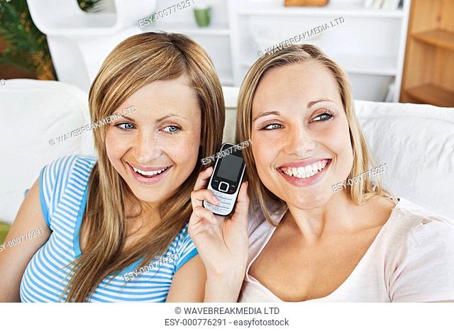 Two bright women using a cellphone at home in the living-room