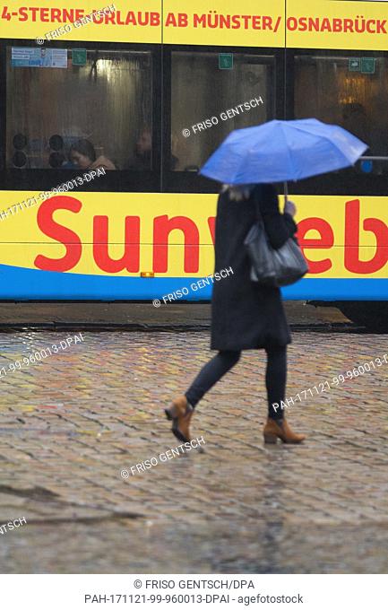 A pedestrian holding an umbrella crosses the street inÂ Muenster, Germany, 21 November 2017. A bus shows an advertisement for holiday in the sun in the...