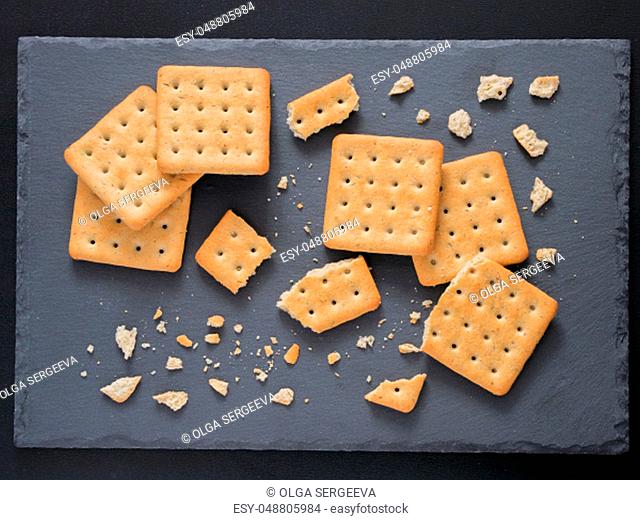 Square crackers with pieces and crumbs on slate gray background. Dry salt cracker cookies with fiber and dry spices. Top view or flat lay