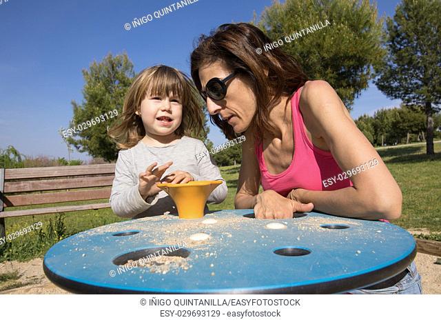 three years old blonde child talking to woman mother and playing with sand in playground at nature Park Valdebebas in Madrid, Spain