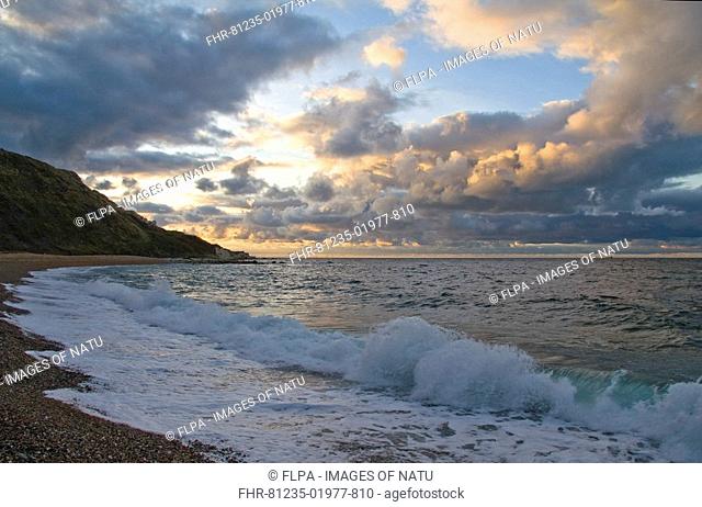 View over English Channel with cumulus clouds and waves breaking on shingle beach at sunrise, Ringstead, Dorset, England, october
