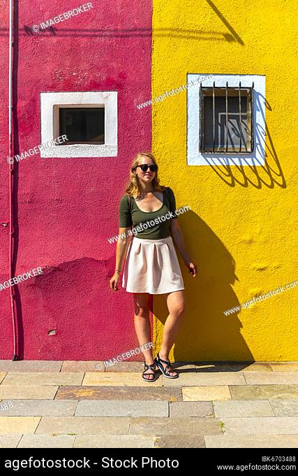 Young woman in front of colorful house, red and yellow house facade, Burano Island, Venice, Veneto, Italy, Europe